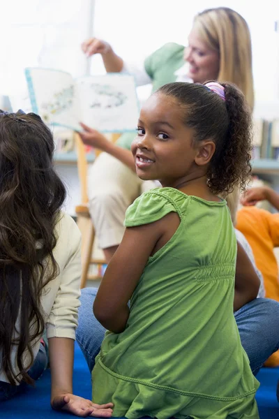 Преподаватель детского сада читает детям в библиотеке, девушка смотрит — стоковое фото