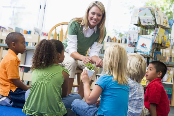 Kindergärtnerin und Kinder betrachten Keimling in Bibliothek — Stockfoto
