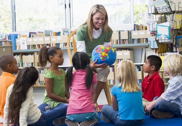 Преподаватель детского сада и дети смотрят на глобус в библиотеке — стоковое фото