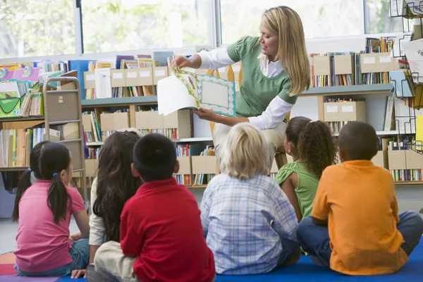 Profesor de jardín de infantes leyendo a los niños en la biblioteca — Foto de Stock
