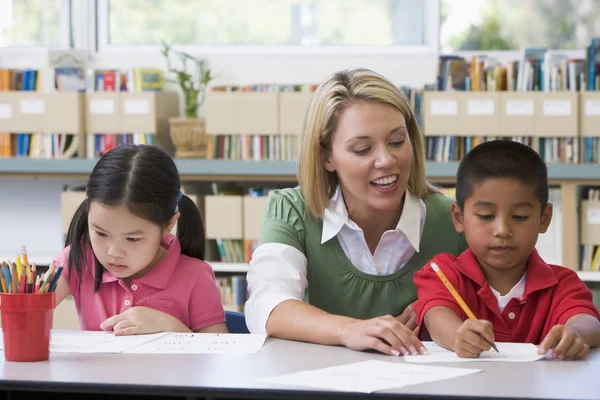 Kindergärtnerin hilft Schülern beim Schreiben Stockbild