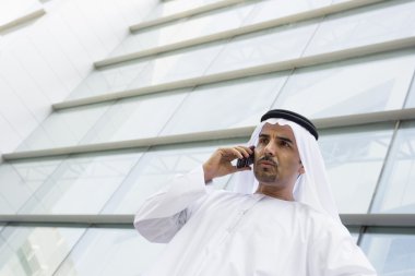 A Middle Eastern businessman talking on the phone outside an off clipart