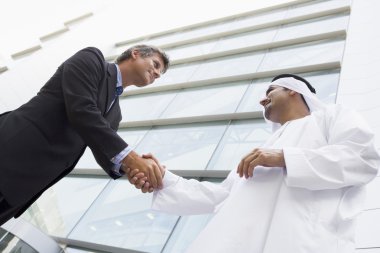 A Middle Eastern businessman and Caucasian man shaking hands out clipart