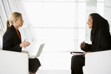 A Middle Eastern and caucasian woman talking at a business meeti clipart