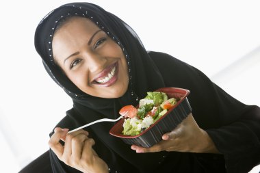 A Middle Eastern woman holding a salad up to the camera clipart