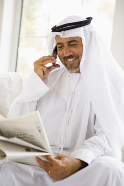 A Middle Eastern man talking on a mobile phone while reading a n clipart