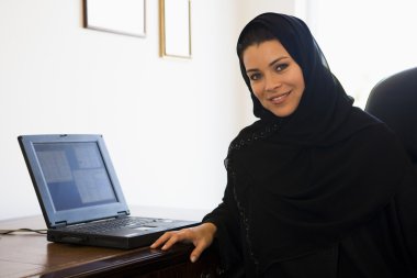 A Middle Eastern woman sitting in front of a computer at home clipart