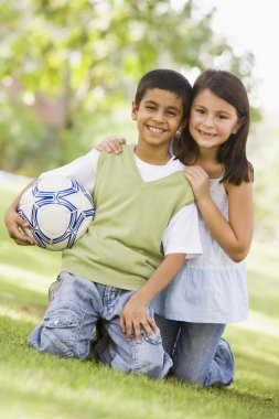 Two children playing football in park looking to camera clipart