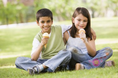 Two children eating ice cream in park clipart