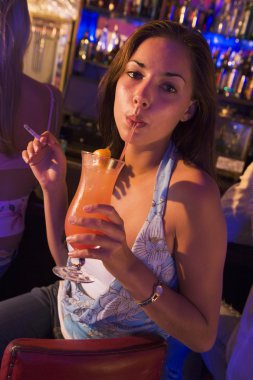 Young woman drinking and smoking at a bar clipart