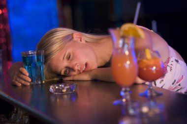 Drunk young woman resting head on bar counter clipart