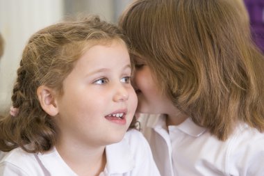 A schoolgirl whispers to her friend in a primary class clipart