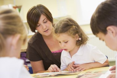 Schoolchildren and their teacher reading in a primary class clipart