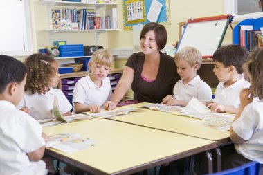 Schoolchildren and their teacher reading in primary class clipart