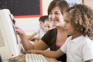 A girl and her teacher working on a computer at primary school clipart