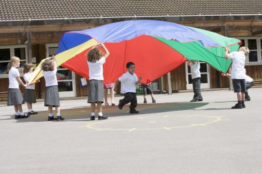 Young children playing with a parachute in a playground clipart