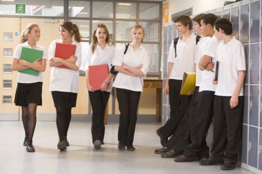 Teenage boys watching girls walk down a school corridor clipart