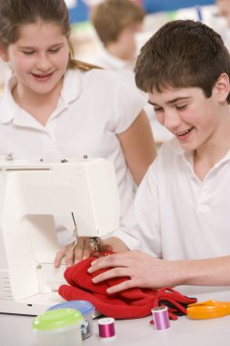 Schoolchildren using a sewing machine in sewing class clipart