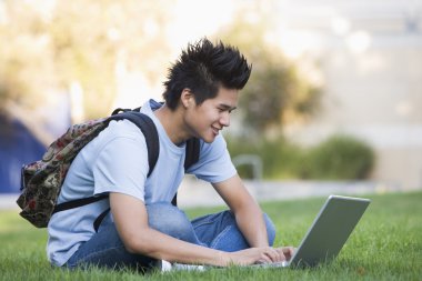 Male university student sitting on grass with laptop clipart