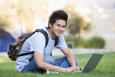 Male student sitting on grass with laptop clipart