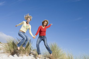 Two young women leaping in air at beach clipart