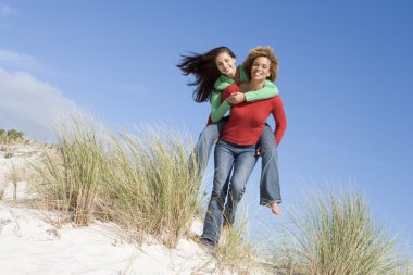 Two friends having piggy back at beach clipart