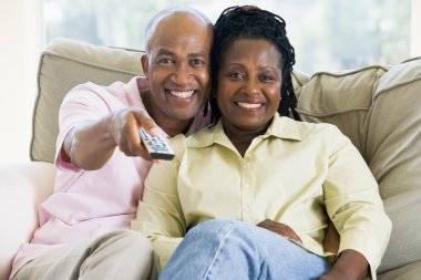 Couple relaxing in living room holding remote control and smilin clipart