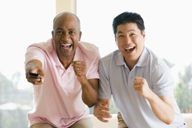 Two men in living room with remote control cheering and smiling clipart