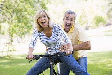 Couple on bike outdoors smiling and acting scared clipart