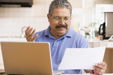 Man in kitchen with laptop and paperwork frustrated clipart