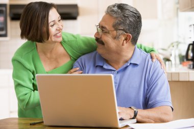 Couple in kitchen with laptop smiling clipart