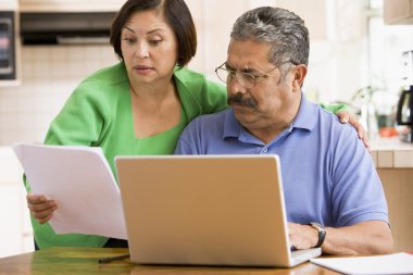 Couple in kitchen with laptop and paperwork clipart