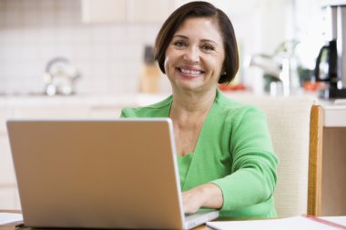 Woman in kitchen with laptop smiling clipart