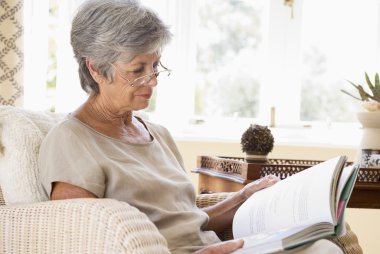 Woman in living room reading book clipart