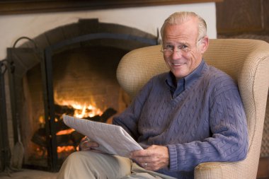 Man sitting in living room by fireplace with newspaper smiling clipart