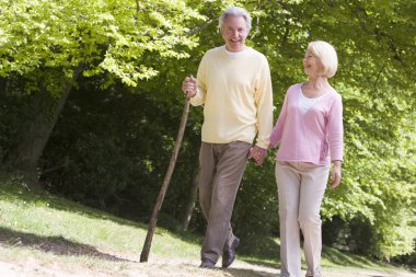 Couple walking on path in park holding hands and smiling clipart