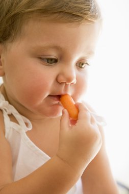 Baby indoors eating carrot. clipart