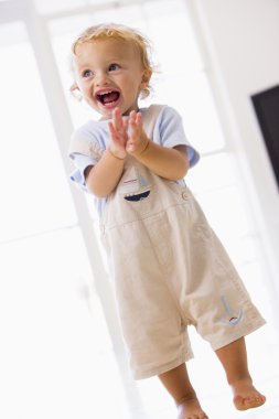 Young boy standing indoors applauding and smiling clipart