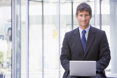 Businessman sitting in office lobby using laptop smiling clipart