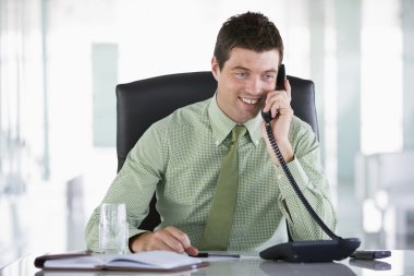 Businessman sitting in office with personal organizer on telepho clipart