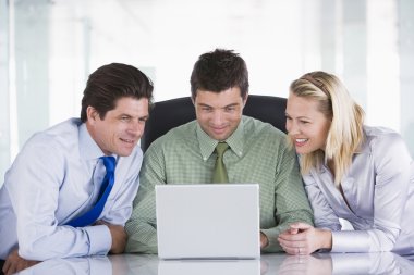 Three businesspeople in office with laptop smiling clipart