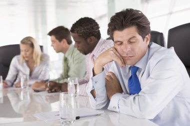 Four businesspeople in boardroom with one businessman sleeping clipart