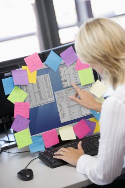 Businesswoman in office pointing at monitor with notes on it clipart