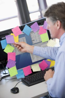 Businessman in office at monitor with notes on it clipart