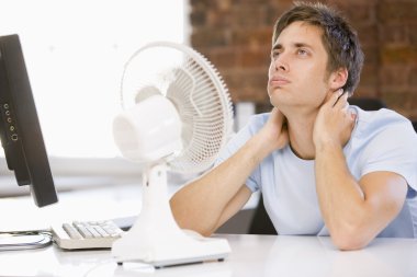 Businessman in office with computer and fan cooling off clipart