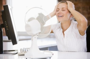 Businesswoman in office with computer and fan cooling off clipart