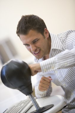 Man sitting in computer room using small punching bag for stress clipart