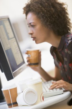 Woman in computer room with many cups of empty coffee around her clipart