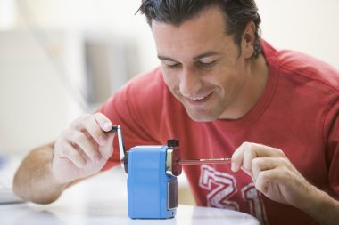 Man indoors using pencil sharpener smiling clipart