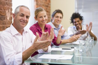 Four businesspeople in boardroom applauding and smiling clipart